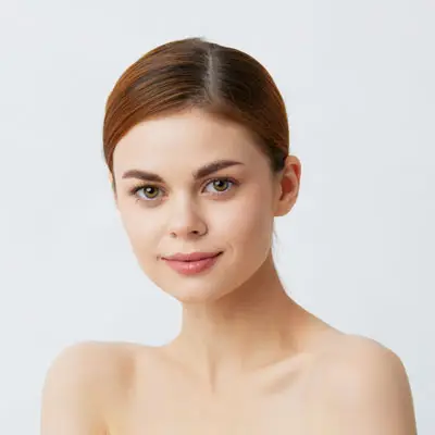 Close-up portrait of a smiling woman with light skin and brown hair tied back on a neutral background.